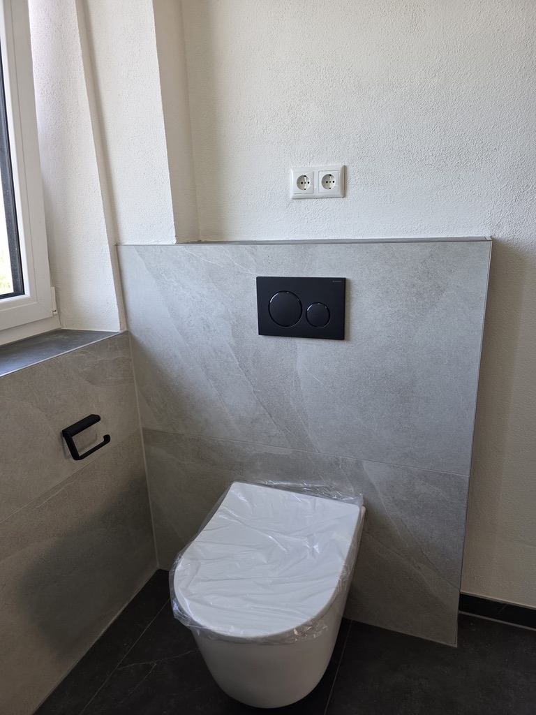 Wand-WC mit schwarzer Betätigungsplatte und Papierhalter